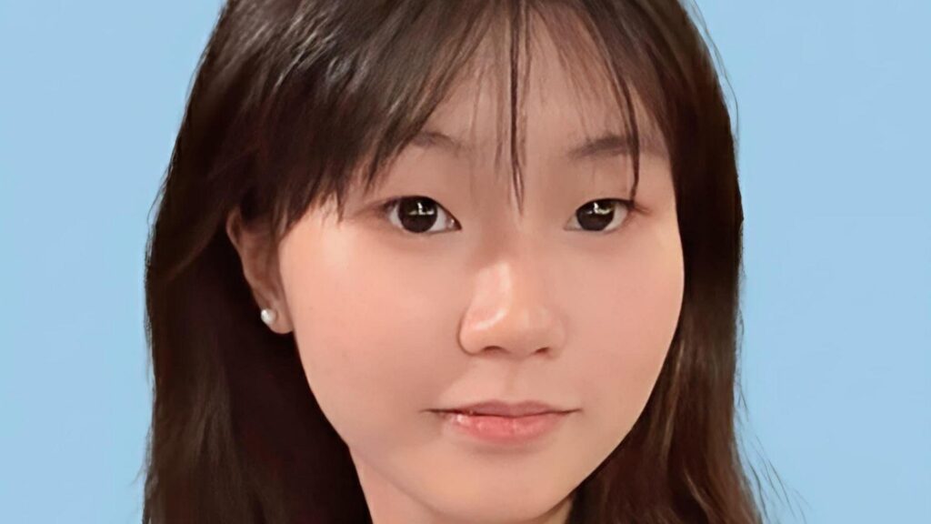 Close-up of a young Chinese girl smiling at the camera, against a blue background