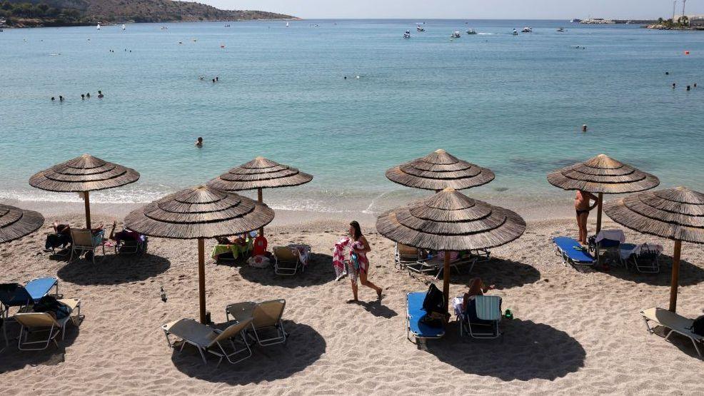 The beach with the sea in the background. There are sun beds and straw shades