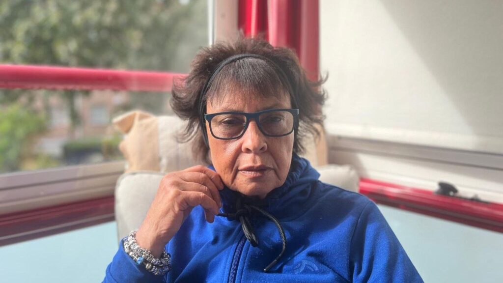 Joyce Thomas wears a blue jumper in a photo taken inside her home in Sweden.