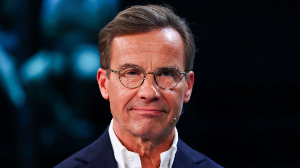 Ulf Kristersson, who has short brown hair and round glasses, poses for the cameras in a TV studio before a debate ahead of the election
