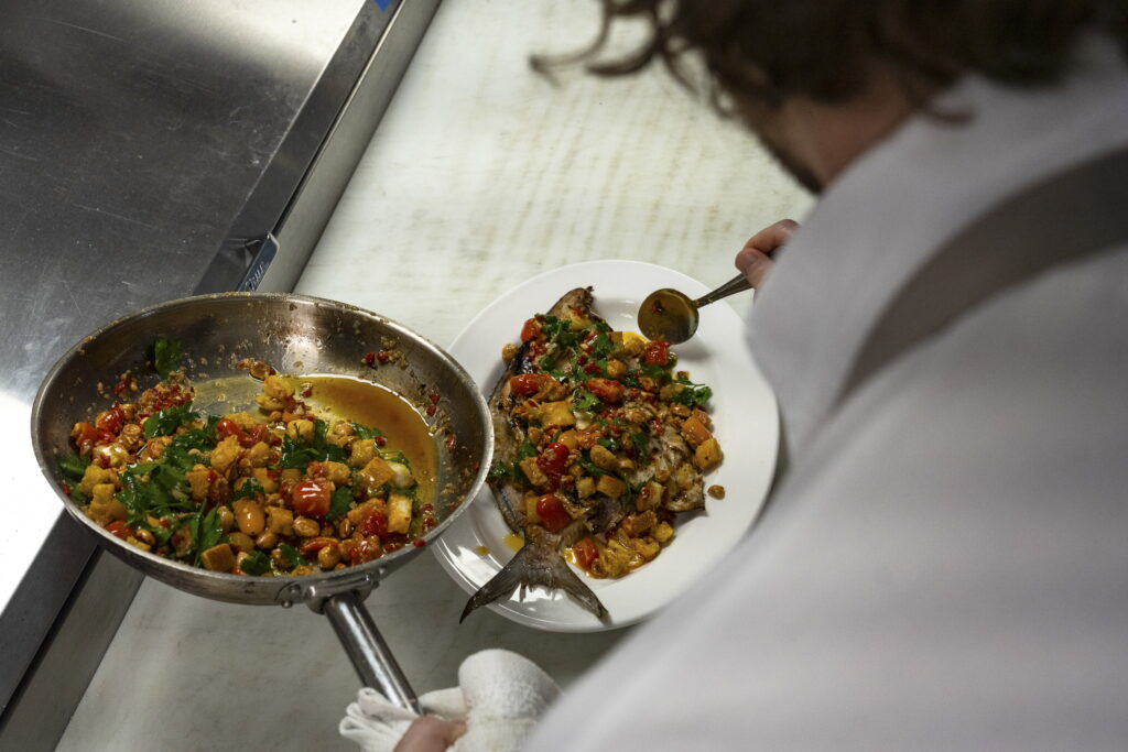 Chef Brian Landry prepares a grilled pompano dish with broken romesco sauce in the kitchen at the Pontchartrain Hotel, explaining its Spanish influences. It