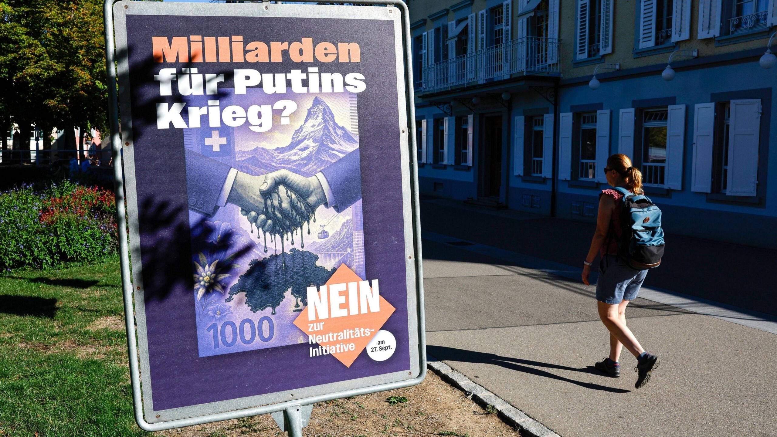 A woman wearing a backpack walks past a placard against the vote on the "Neutrality Initiative" in Rheinfelden, Switzerland
