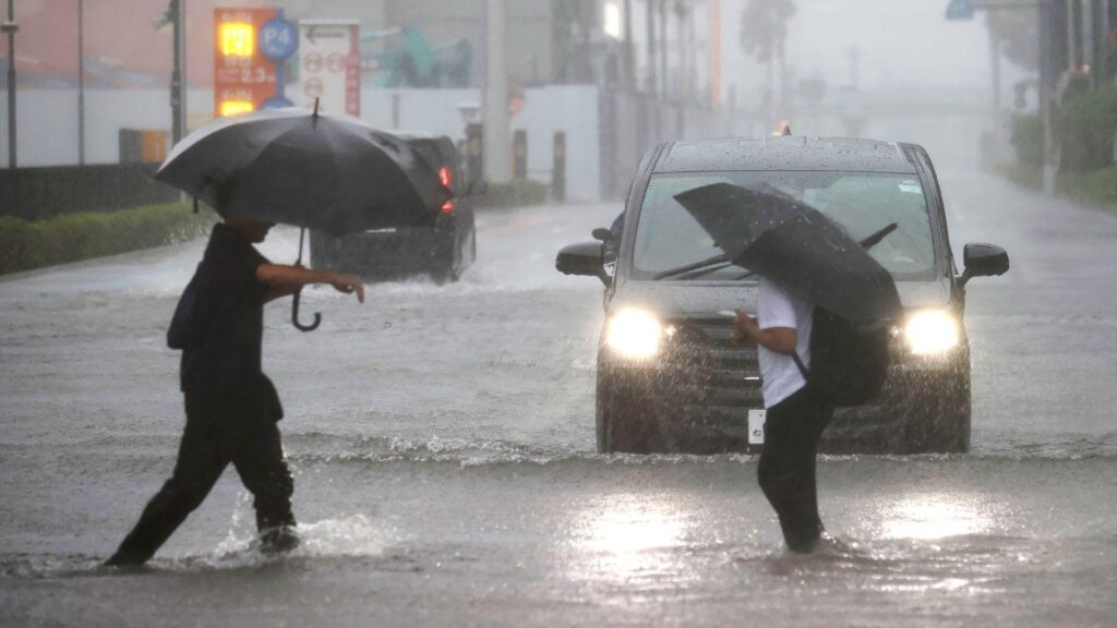 Two men with umbrellas are ankle-deep in water as they cross a road in Funabashi, Chiba Prefecture, Japan