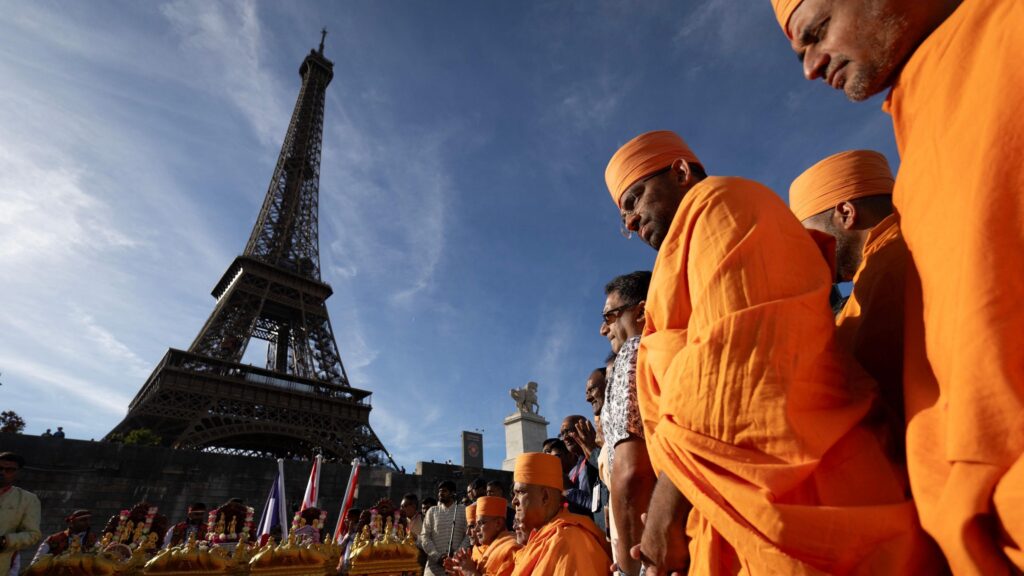 Hindu monks stand in front of the Eiffel Tower wearing traditional orange robes.