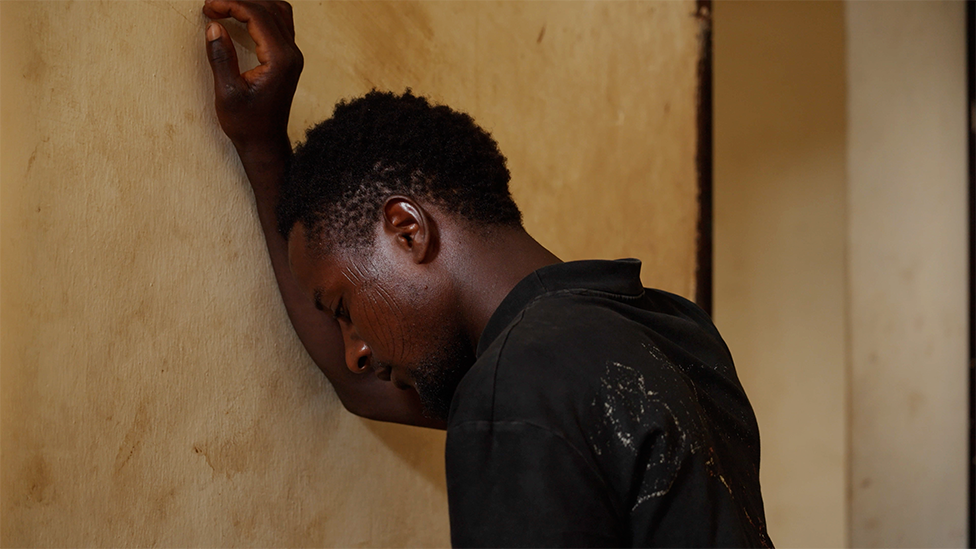 Usman Muhammad leans against a wall with his head resting on his forearm.