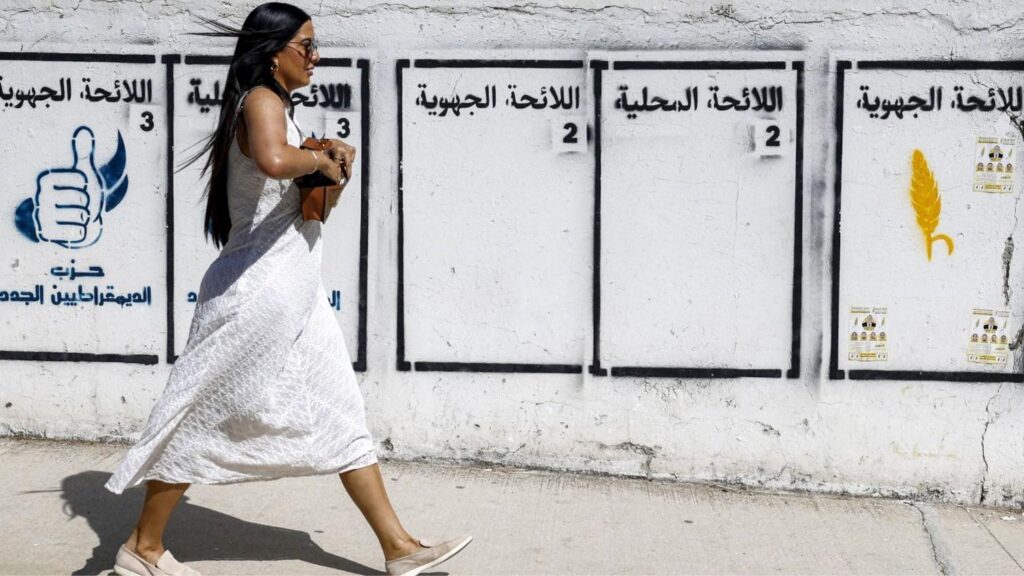 A woman walking by a wall in Tangiers with the electoral symbols of political parties painted on it.