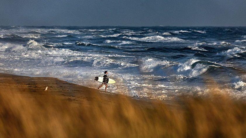 A man carries a surfboard on a beach