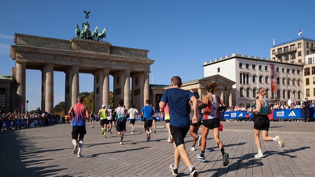 A dozen runners seen from behind as the run towards the Brandenburg Gate in Berlin during the Berlin Marathon