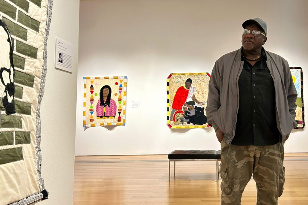 Gary Tyler speaks about his work at the Grand Rapids Art Museum in Michigan. Behind Tyler are his quilts Big Toe, (2024) and Enduring, (2025). They feature two individuals who are incarcerated. He hopes his work draws attention to their plight and humanity.