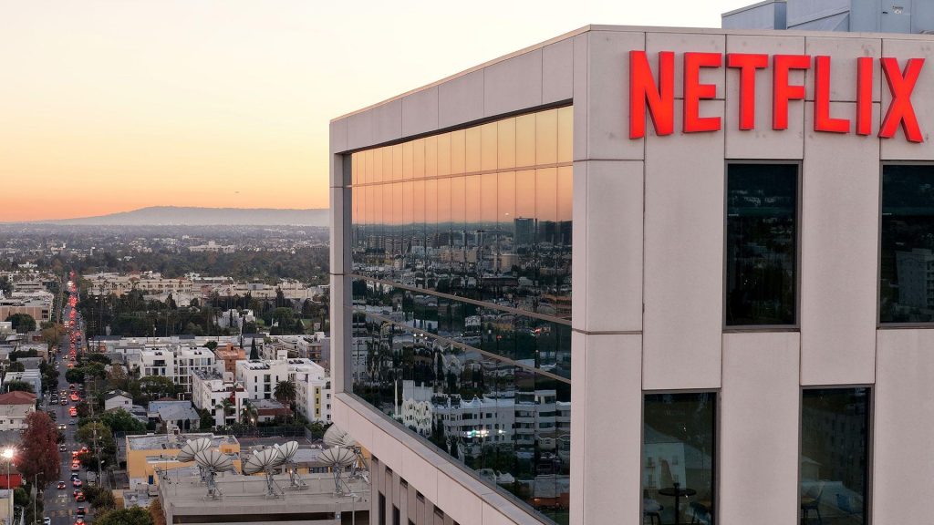 A wide view shows the Netflix logo on the side of a cream coloured building at Netflix studios in 2025 in LA, with the iconic LA skyline in the background at sunset.