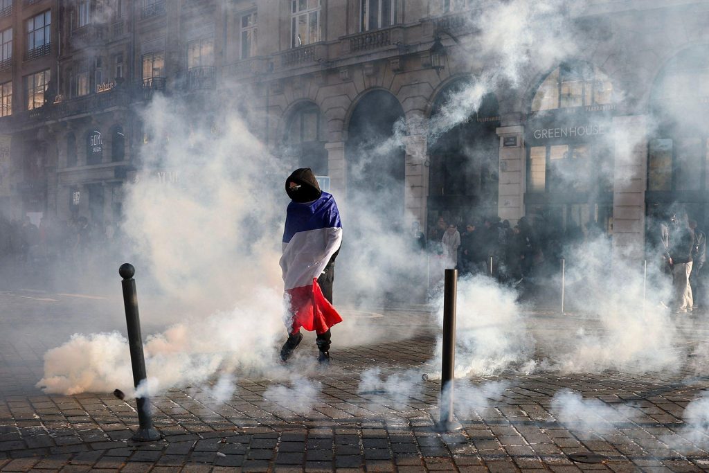 A protester wrapped in a French flag stands with smoke all around on a street in Lille on 17 October.