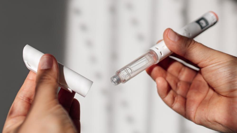 A womans hands hold a weight loss injection pen.