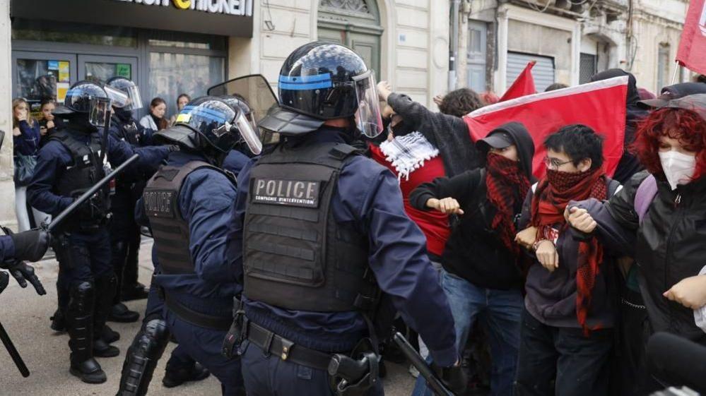 Masked students face riot police in full armour in the streets