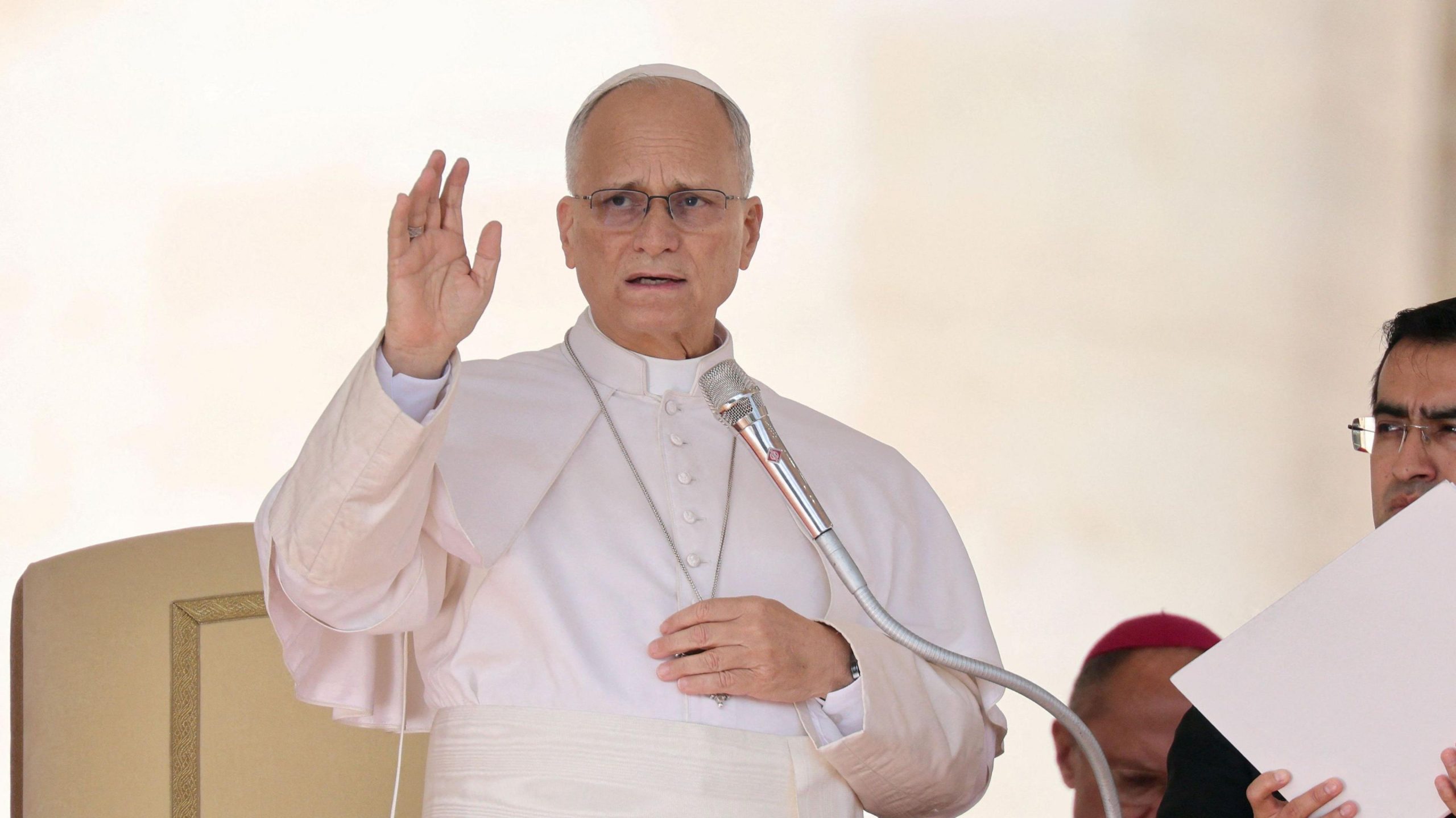 Pope Leo speaks into a microphone and raises his hand