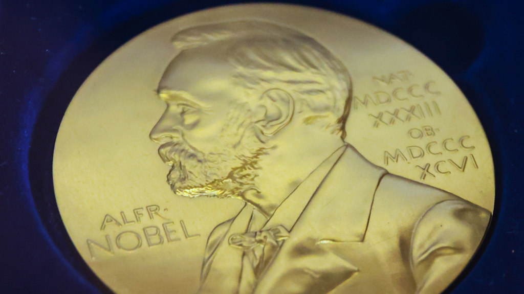 Gold medal in blue background with a picture of Nobel sketched out of the coin and roman numerals on the right.