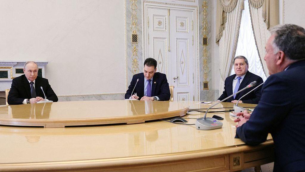 Vladimir Putin (L) sits at a large table with foreign policy aide Yuri Ushakov (second right), Steve Witkoff (R) and one other man